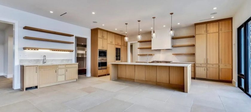 Open kitchen with light oak cabinets, floating shelves, pendant lights, and a long island